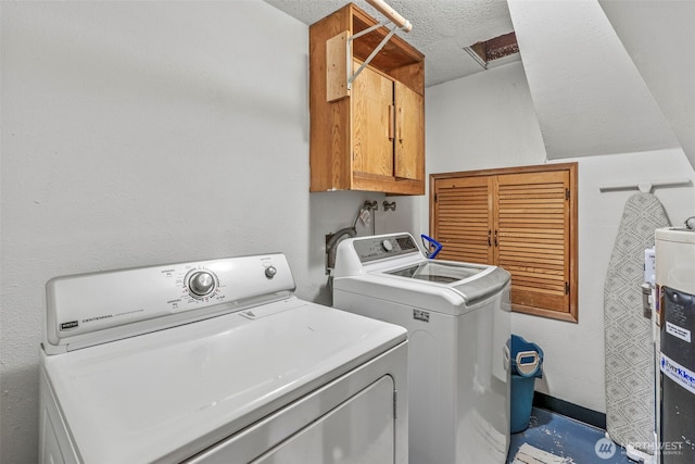 laundry area featuring washing machine and clothes dryer, cabinet space, electric water heater, and a textured ceiling