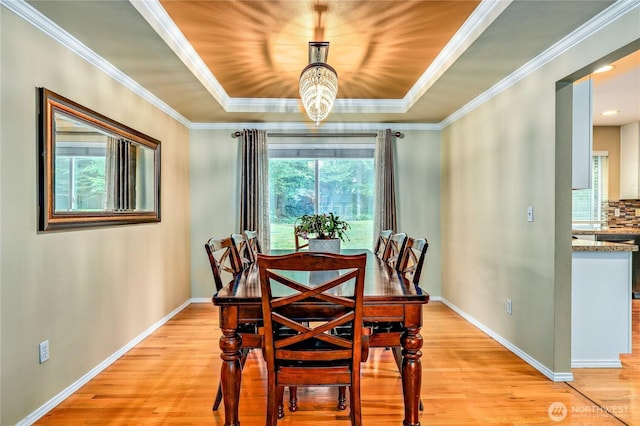 dining area with light wood-style floors, crown molding, a tray ceiling, baseboards, and a chandelier