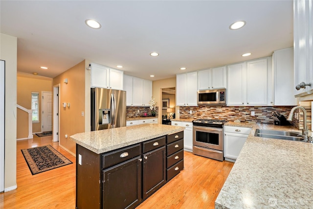 kitchen featuring appliances with stainless steel finishes, a sink, white cabinets, a center island, and light countertops