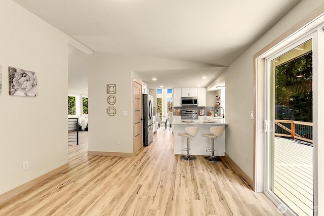 9630 SE Driftwood Dr, Port Orchard, WA 98367 - kitchen with stainless steel appliances, a breakfast bar area, white cabinets, light wood-style flooring, and lofted ceiling