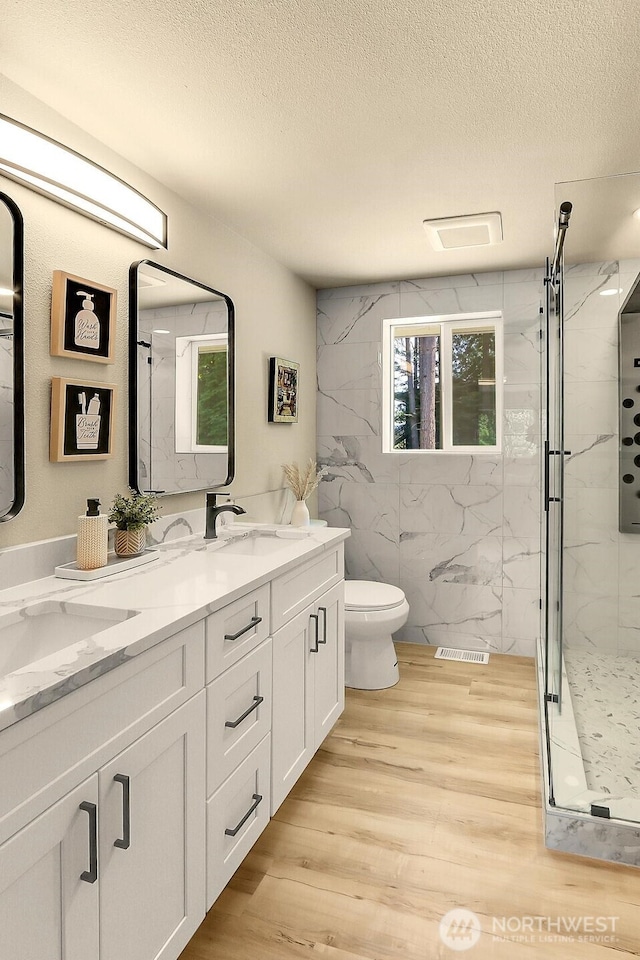 9630 SE Driftwood Dr, Port Orchard, WA 98367 - full bathroom featuring a marble finish shower, a textured ceiling, toilet, wood finished floors, and double vanity