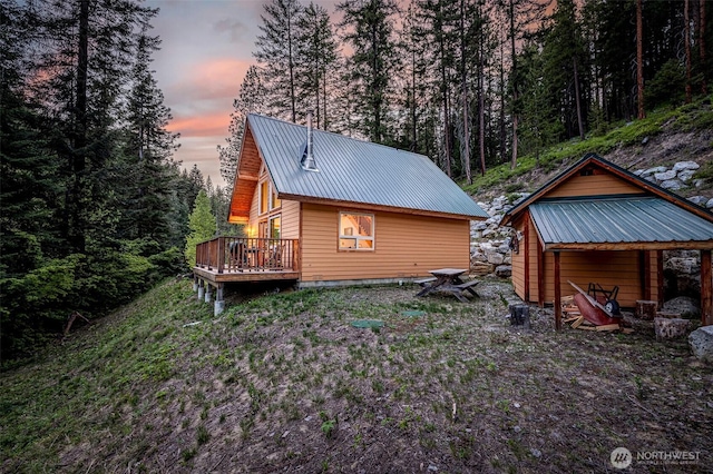 view of home's exterior with a wooden deck, metal roof, and a wooded view