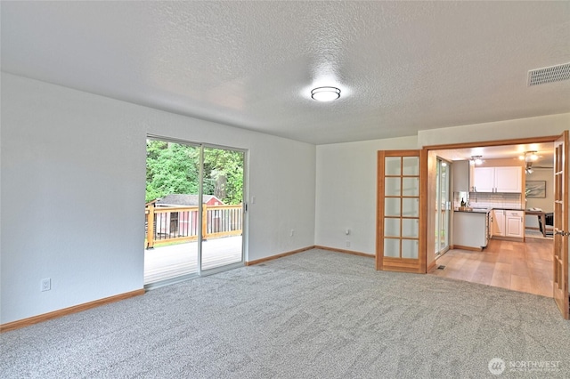 unfurnished living room with light carpet, a textured ceiling, baseboards, and french doors