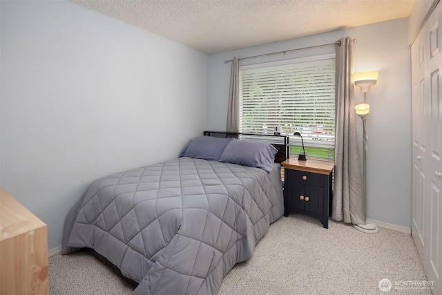 bedroom featuring light carpet, a textured ceiling, and baseboards