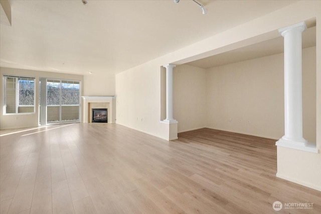 unfurnished living room featuring ornate columns, a glass covered fireplace, and wood finished floors