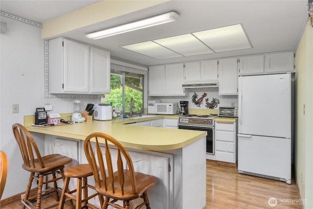 kitchen featuring white appliances, under cabinet range hood, a peninsula, a sink, and light countertops
