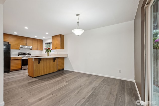 35010 45th Ave S, Auburn, WA 98001 - kitchen with stainless steel electric range oven, freestanding refrigerator, under cabinet range hood, brown cabinetry, and a kitchen bar