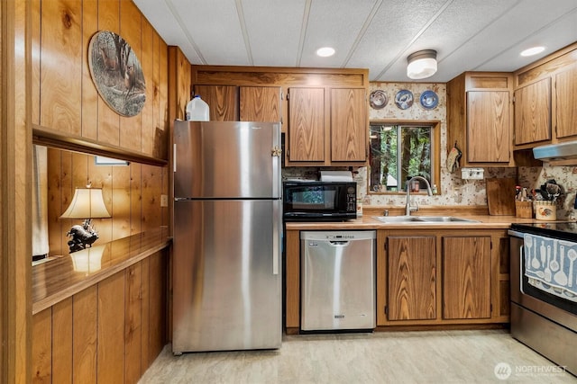 kitchen with appliances with stainless steel finishes, a sink, brown cabinets, light countertops, and under cabinet range hood
