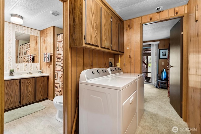 laundry area with separate washer and dryer, wood walls, a textured ceiling, a sink, and light colored carpet