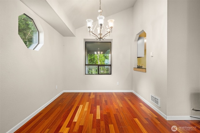 unfurnished dining area featuring a chandelier, healthy amount of natural light, wood finished floors, baseboards, and vaulted ceiling