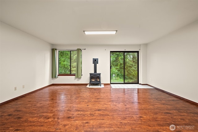 unfurnished living room with a wood stove, light wood-type flooring, and baseboards