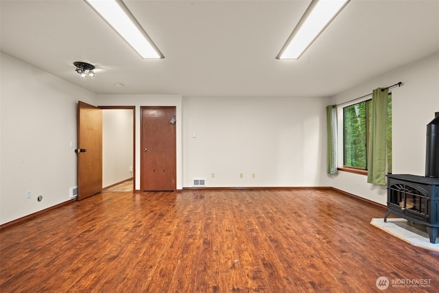 unfurnished living room featuring a wood stove, wood finished floors, and baseboards