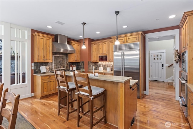 12916 318th Ave NE, Duvall, WA 98019 - kitchen featuring wall chimney range hood, light wood-style floors, a center island with sink, tasteful backsplash, and recessed lighting