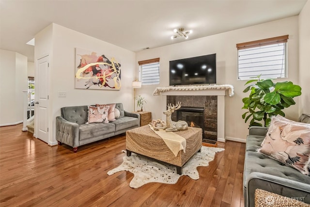 living area with wood finished floors, a tiled fireplace, plenty of natural light, and baseboards