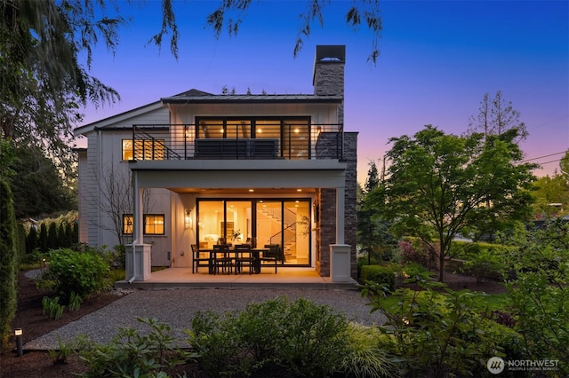 back of property at dusk featuring a balcony, a chimney, and a patio area