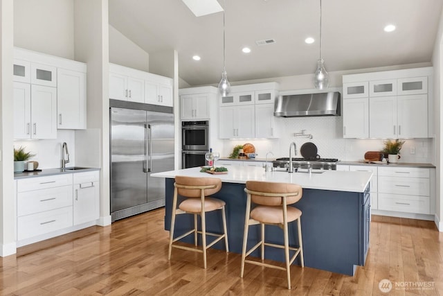 5754 W 26th Crst, Ferndale, WA 98248 - kitchen with appliances with stainless steel finishes, wall chimney exhaust hood, backsplash, vaulted ceiling, and a kitchen island with sink