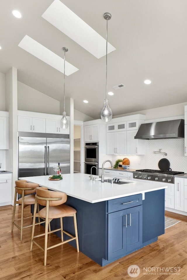 5754 W 26th Crst, Ferndale, WA 98248 - kitchen with wall chimney range hood, stainless steel appliances, a sink, white cabinetry, and a skylight