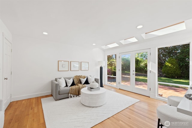 living area featuring a skylight, light wood finished floors, recessed lighting, and baseboards