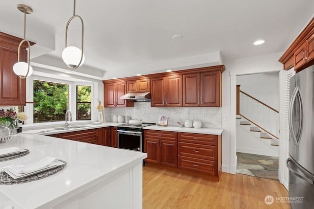kitchen with under cabinet range hood, stainless steel appliances, a sink, light countertops, and decorative backsplash