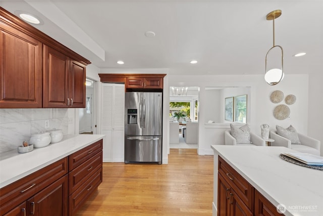 kitchen featuring stainless steel refrigerator with ice dispenser, light wood-style flooring, backsplash, recessed lighting, and decorative light fixtures