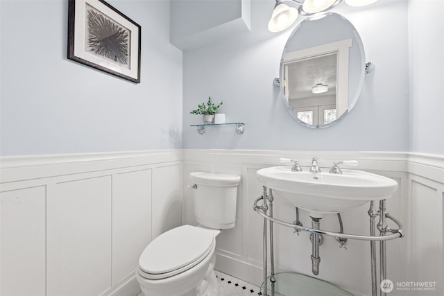 half bath featuring wainscoting, toilet, and a decorative wall