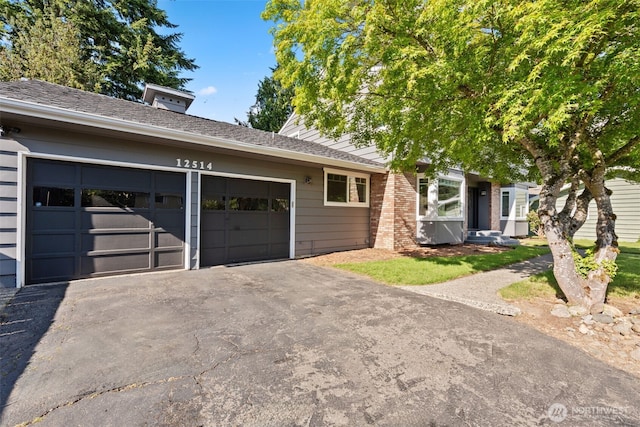 view of front of house featuring driveway, an attached garage, and a shingled roof