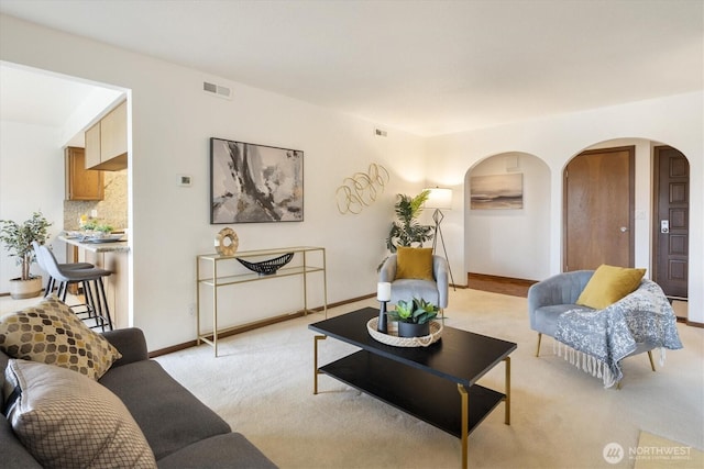 living room featuring arched walkways, light colored carpet, and baseboards