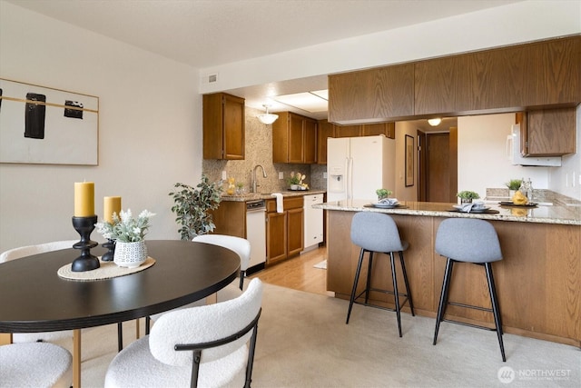 kitchen featuring white appliances, a peninsula, brown cabinets, tasteful backsplash, and a breakfast bar