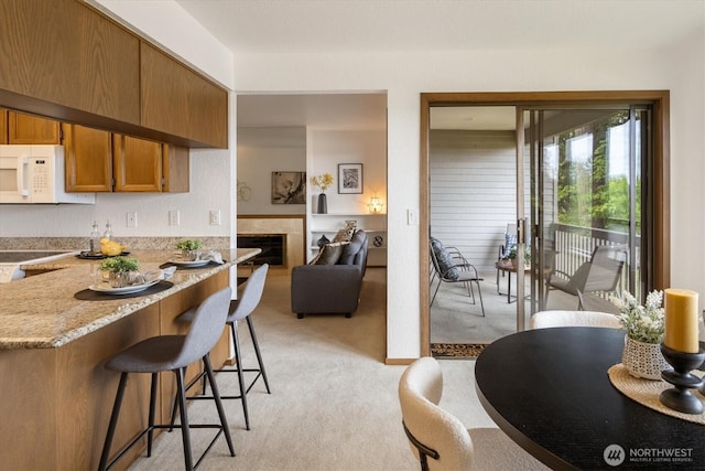 kitchen featuring light colored carpet, white microwave, brown cabinets, a kitchen breakfast bar, and a fireplace