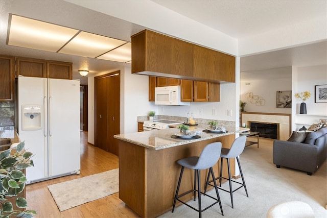 kitchen featuring white appliances, brown cabinetry, light wood-style flooring, a peninsula, and a breakfast bar area