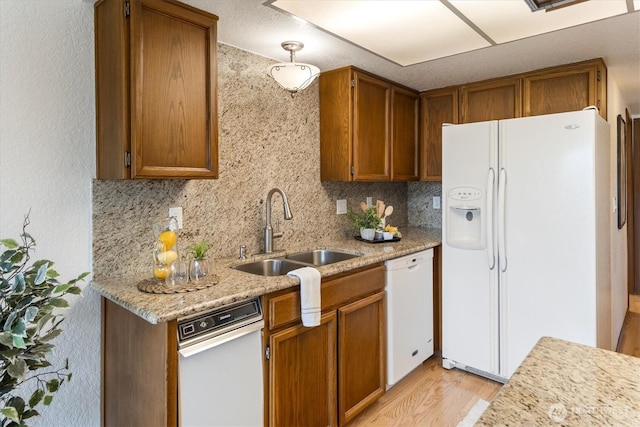 kitchen featuring white appliances, a sink, light wood-style flooring, and brown cabinetry
