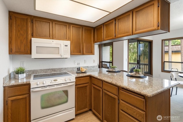 kitchen featuring white appliances, a peninsula, brown cabinetry, and light stone counters