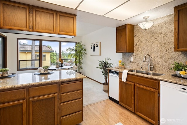 kitchen with white dishwasher, a sink, tasteful backsplash, brown cabinets, and light wood-style floors