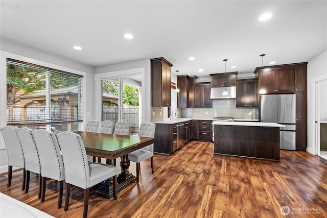 6410 83rd Avenue Ct W, University Place, WA 98467 - kitchen with freestanding refrigerator, dark brown cabinetry, light countertops, under cabinet range hood, and tasteful backsplash