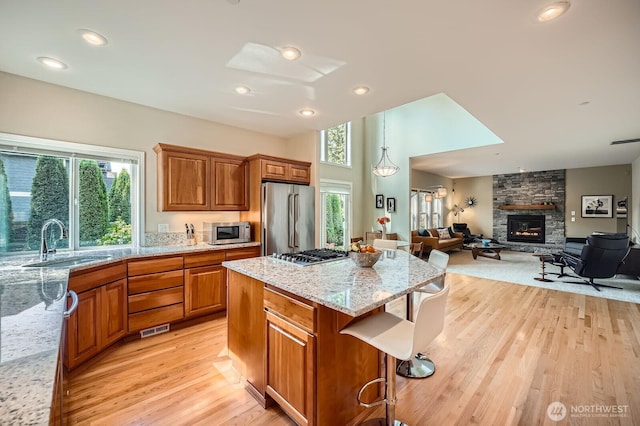922 Chelan Ave NE, Renton, WA 98059 - kitchen featuring appliances with stainless steel finishes, a stone fireplace, light wood-type flooring, a sink, and brown cabinets