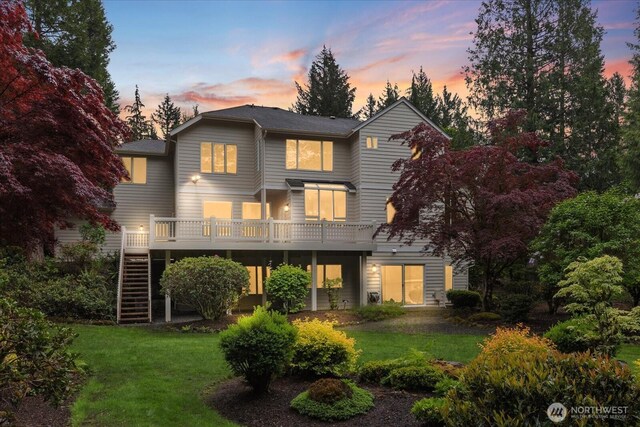 back of house at dusk featuring stairway, a yard, and a wooden deck