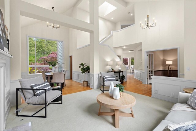 living room featuring a chandelier, a decorative wall, light wood-style flooring, a wainscoted wall, and high vaulted ceiling