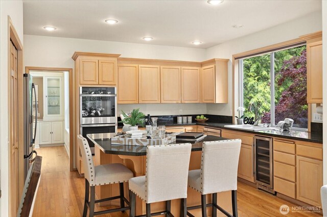 kitchen featuring light brown cabinets, beverage cooler, stainless steel appliances, a sink, and dark countertops