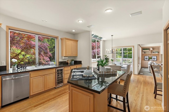 kitchen featuring appliances with stainless steel finishes, a sink, wine cooler, light brown cabinets, and a kitchen island