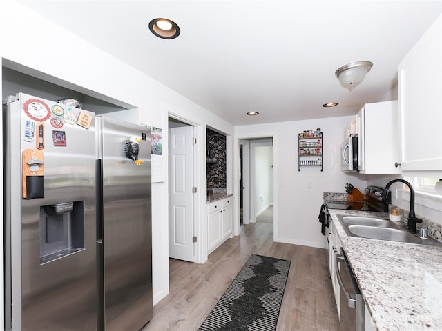 kitchen featuring stainless steel appliances, a sink, white cabinetry, light wood-style floors, and light stone counters