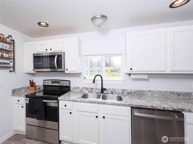 kitchen with appliances with stainless steel finishes, a sink, white cabinets, light stone countertops, and recessed lighting