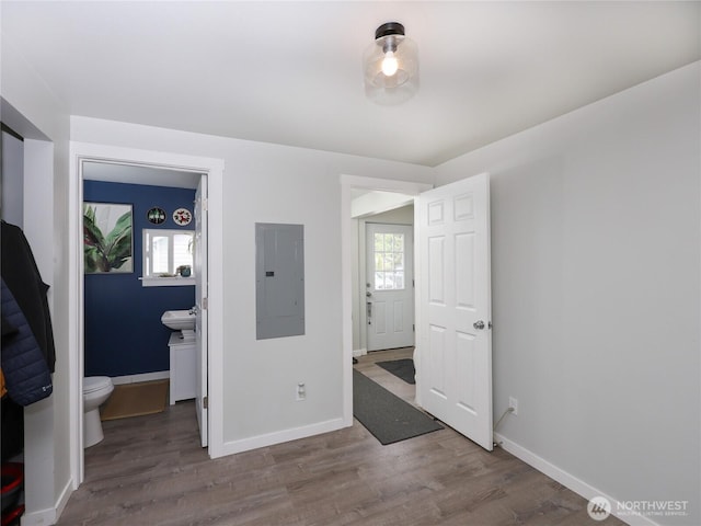 unfurnished bedroom featuring electric panel, wood finished floors, baseboards, and ensuite bathroom