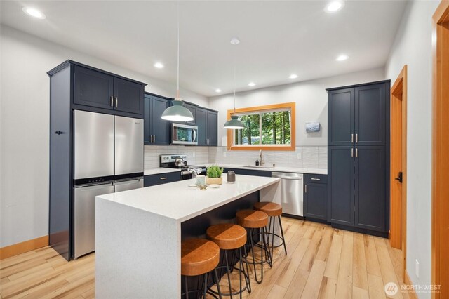 7467 Canyon View Dr, Deming, WA 98244 - kitchen featuring appliances with stainless steel finishes, a breakfast bar, light wood-style flooring, decorative backsplash, and light countertops