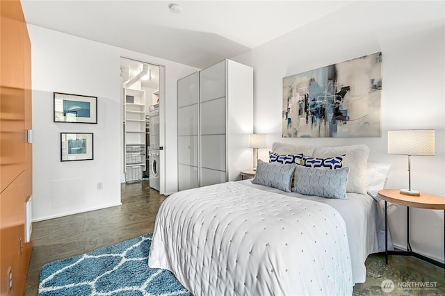 bedroom with stacked washer and clothes dryer, a walk in closet, wood finished floors, and baseboards