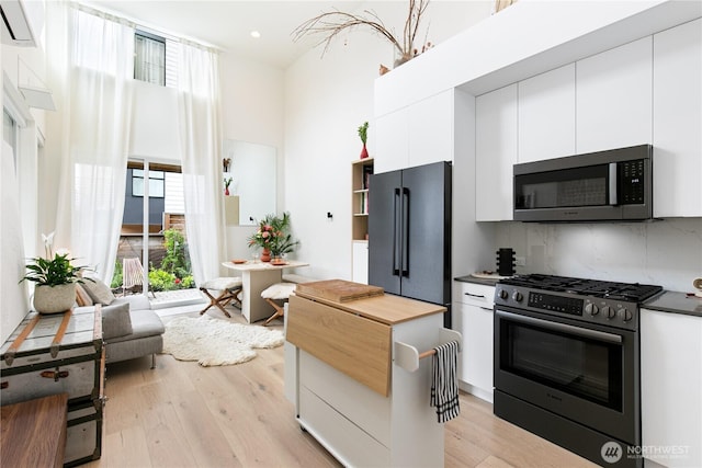 916NW 56th St Unit G, Seattle, WA 98107 - kitchen featuring appliances with stainless steel finishes, white cabinetry, light wood-type flooring, backsplash, and a high ceiling