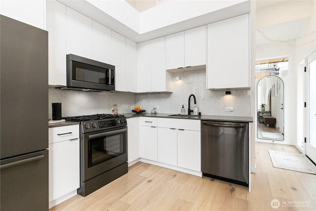 916NW 56th St Unit G, Seattle, WA 98107 - kitchen featuring stainless steel appliances, a sink, light wood finished floors, dark countertops, and decorative backsplash