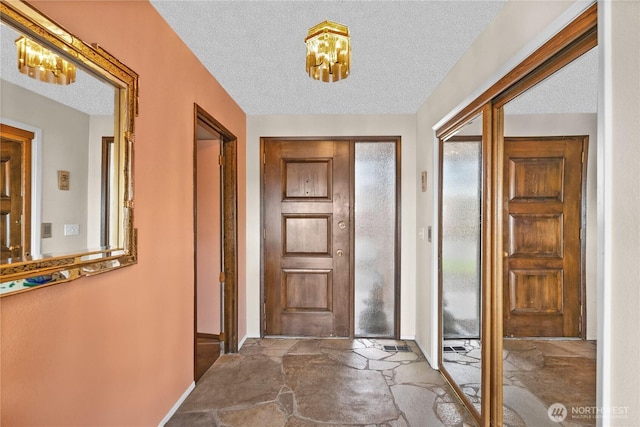 7618 19th St W, Tacoma, WA 98466 - foyer entrance featuring a chandelier, stone finish flooring, a textured ceiling, and baseboards