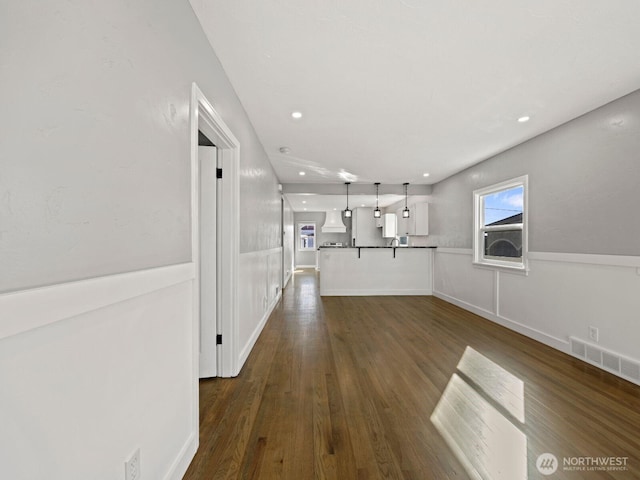 corridor with dark wood finished floors, recessed lighting, and a wainscoted wall