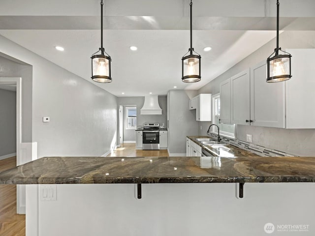kitchen featuring stainless steel range with electric cooktop, a sink, custom exhaust hood, dark stone counters, and baseboards