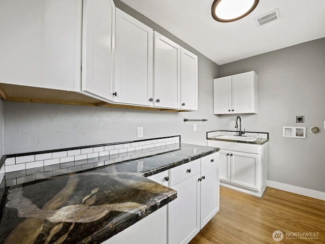 kitchen with white cabinets, light wood-style flooring, dark stone countertops, a sink, and baseboards